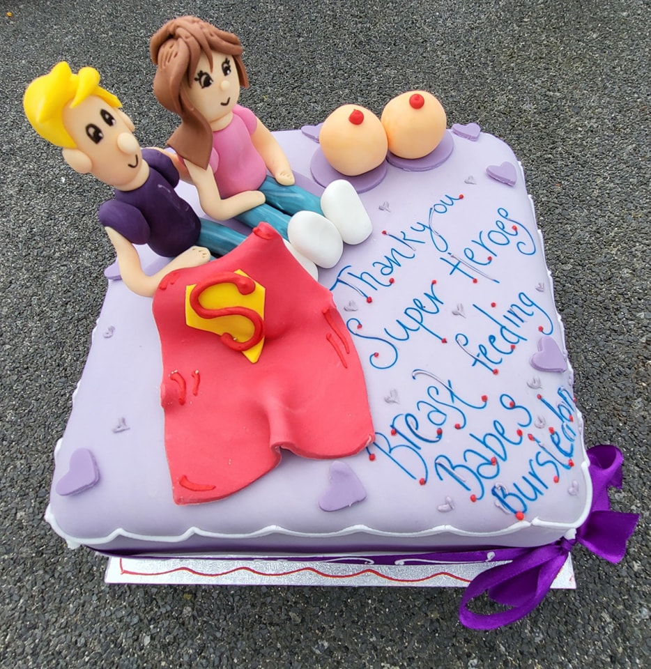 Square cake covered with purple fondant icing, on top are a man and a woman made out of fondant with a superhero cape and a pair of boobs. The writing on the cake says thank you super heroes, Breatfeeding Babes Bursledon.